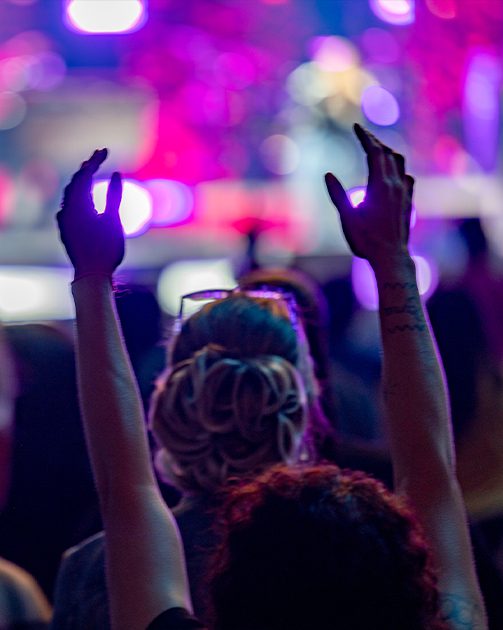 a shot of an indoor worship service with everything out of focus except for two hands extended towards the sky