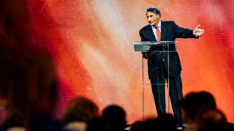 Dr. Youssef speaking onstage with arms outstretched, looking towards audience