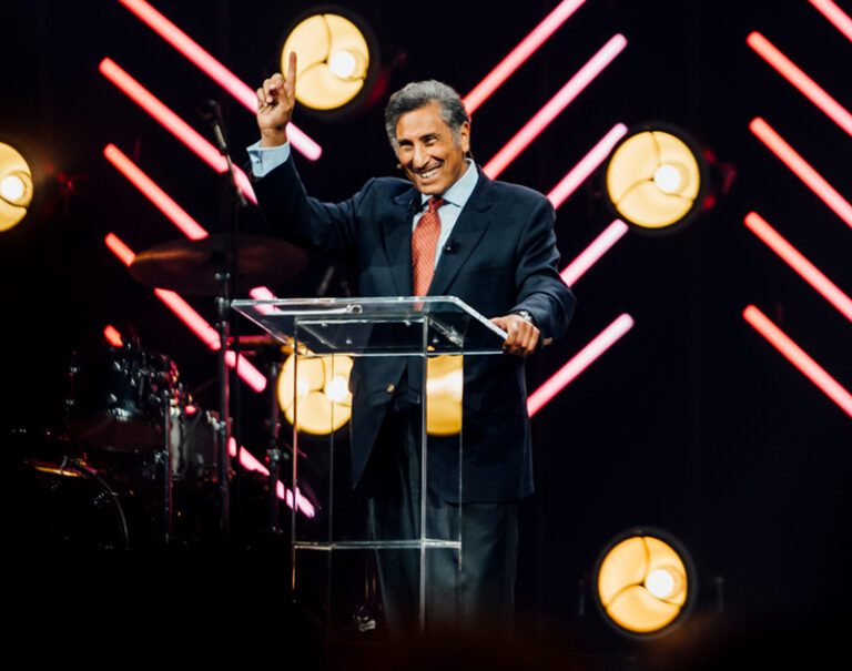 Dr. Youssef smiling and speaking at a podium with colorful lights behind