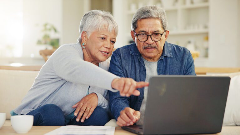 an elderly woman and man pointing towards and looking at a laptop screen together