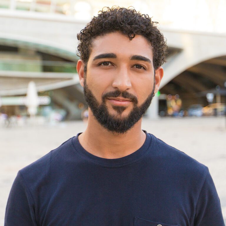 close up of young man in a navy sweater softly smiling, looking at the camera