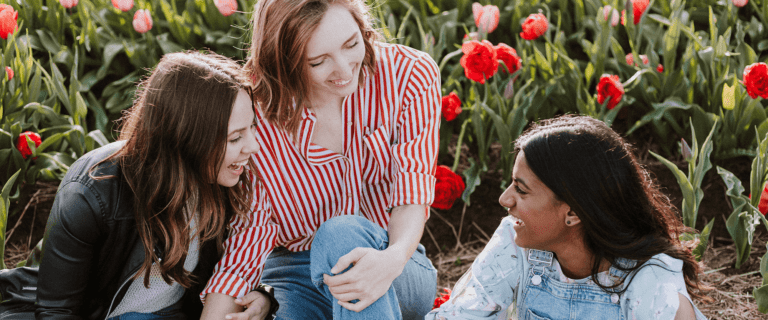 Three young women laugh among flowers