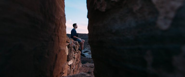 A man is shown through a crevasse, sitting on a stone wall