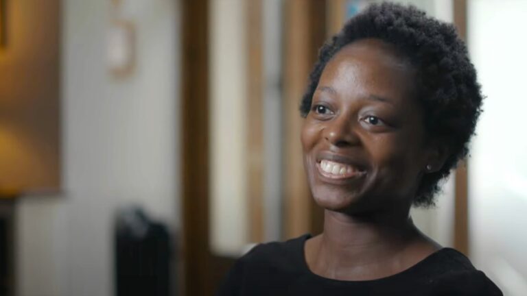 A woman smiles and looks to the side of the camera