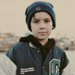 School age boy standing with a jacket and hat