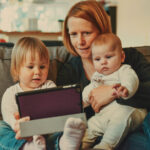 Mother with two babies in her lap looking at a tablet