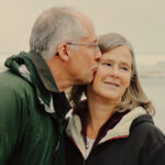 Senior couple standing. Husband gives wife a kiss
