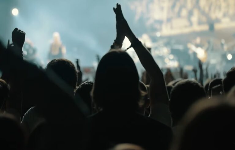 Crowd at a worship event, with raised hands and stage lights in the background.