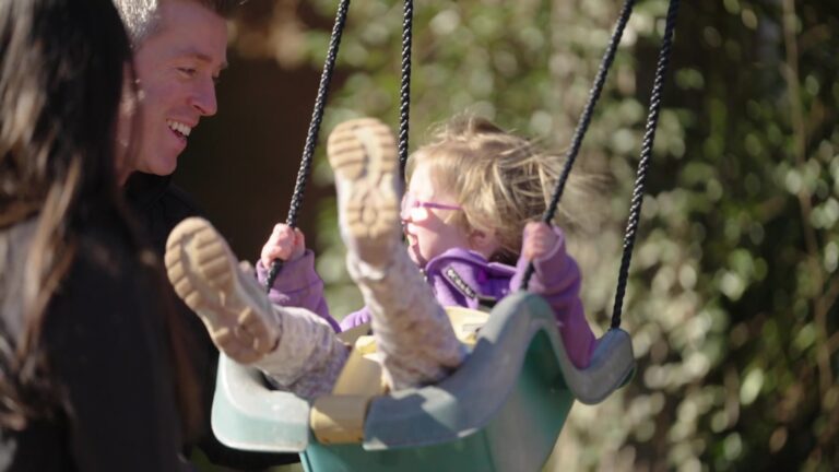 Man playing with his young daughter on a swing set