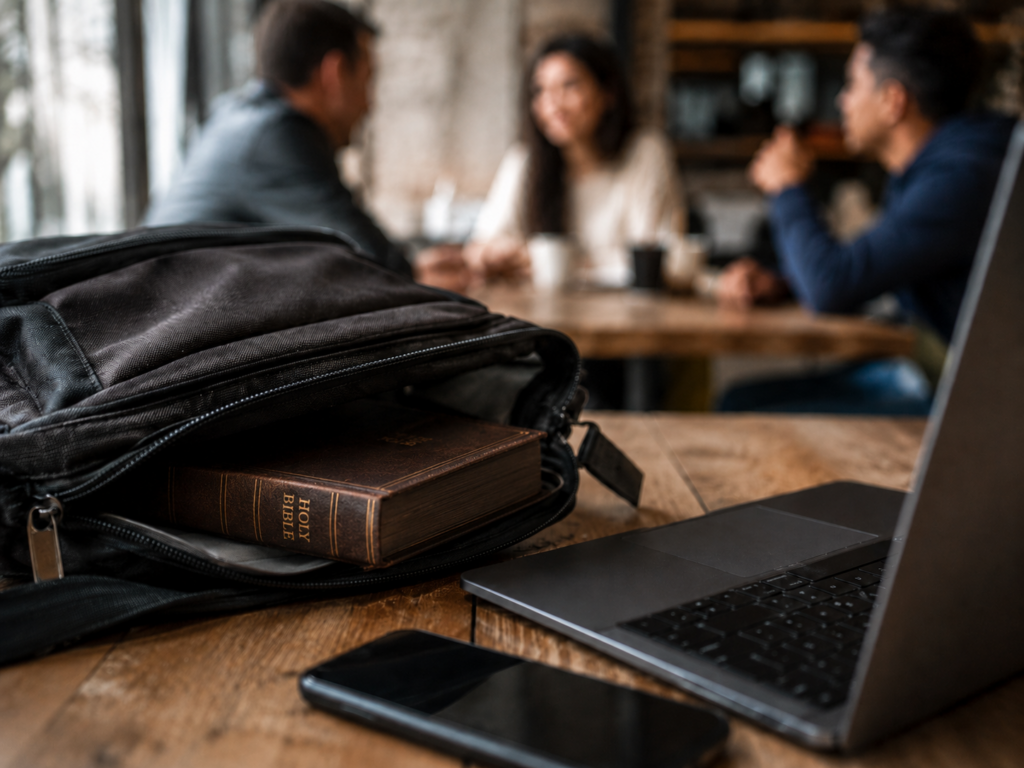 Bible partially tucked inside a backpack beside a laptop in a café, symbolizing Christian faith kept private in everyday life.