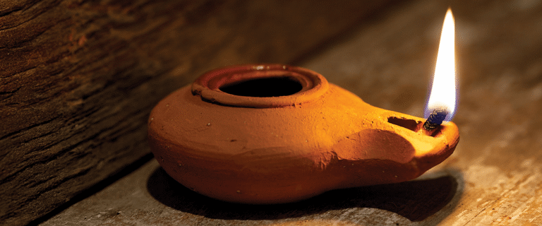 A lit clay oil lamp glows warmly on a wooden surface.