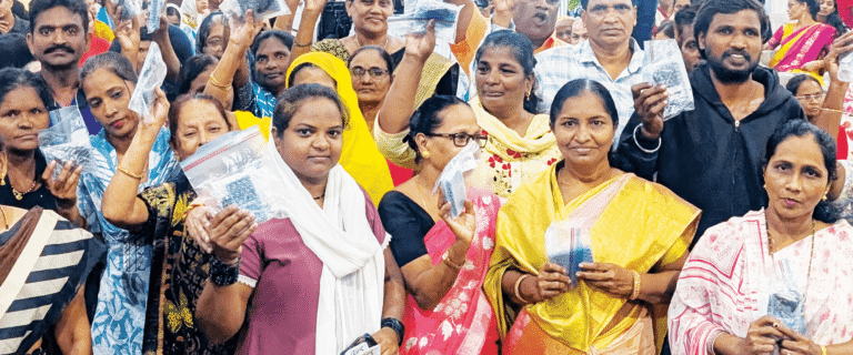 A crowd of men and women in India proudly hold up bags of Gospel outreach materials during a community ministry event.