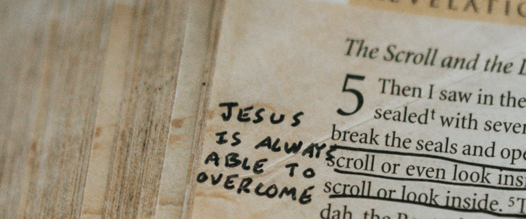 Close-up of an open Bible turned to Revelation chapter 5, with verses underlined and a handwritten note reading, “Jesus is always able to overcome.”