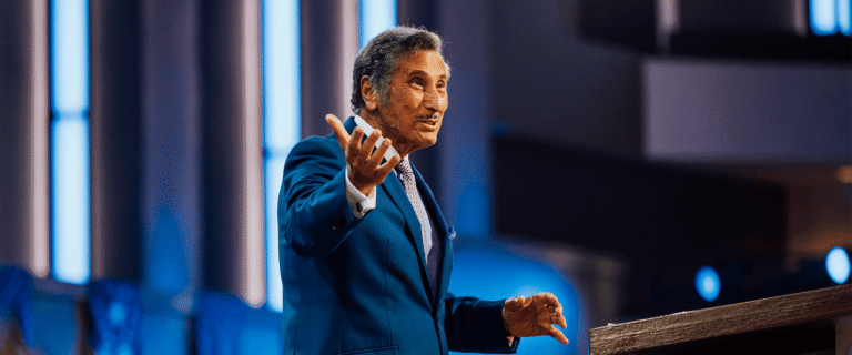 Dr. Michael Youssef speaks onstage, gesturing to the audience from behind a podium.