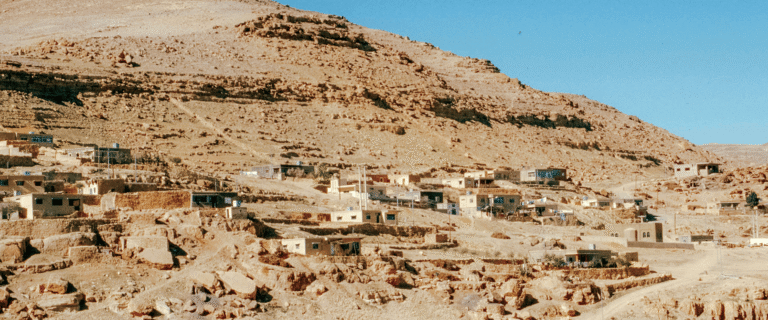 A small village sits along a rocky, arid mountainside beneath a clear blue sky.